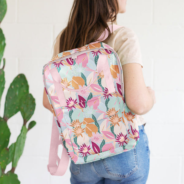 Girl holding a colorful floral collage patterned vegan leather backpack over her shoulder.