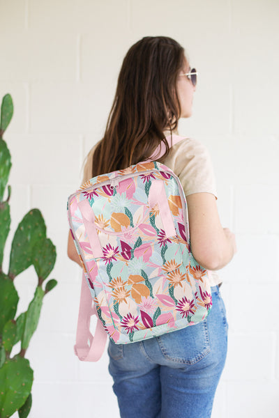 Girl holding a colorful floral collage patterned vegan leather backpack over her shoulder.