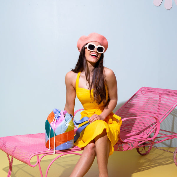 Girl in yellow dress sitting with a a wavy block colored bucket bag. 