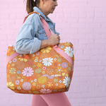 girl carrying large cooler bag with floral print on brown background with peach webbing handles
