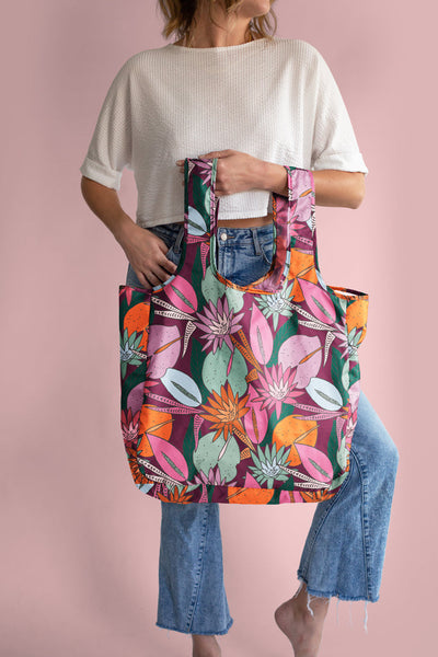 Lady in white top holding a large Floral Nights twist and shout reusable tote with a jewel tone floral collage pattern.