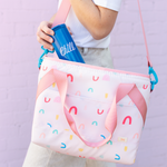 Cute soft cooler bag in pink with rainbows over a girls shoulder putting a beverage holder in