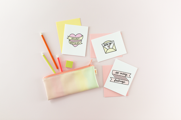 No regrets card set laying on a light pink table. Light daybreak gradient pouch with pencils laying next to it. 