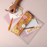 Girl writing on cute colorful stationery kit with a pouch that has a floral print, three jotter pens and a set of letterpress greeting cards with flower art and complementary envelopes.