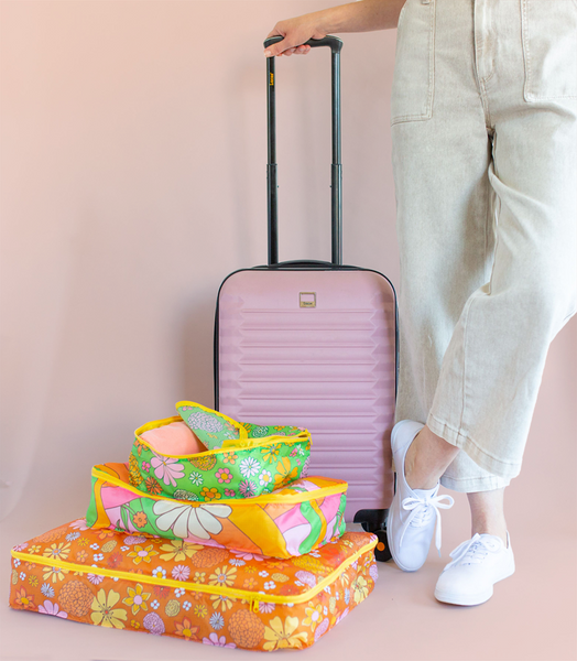 Flower power packing cubes stacked largest to smallest with woman holding pink suitcase.