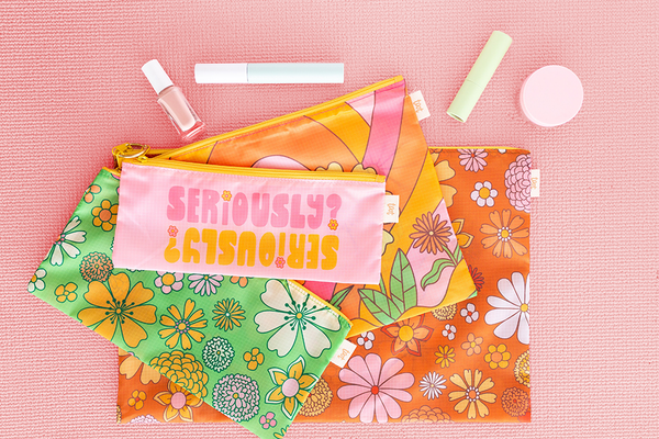 four different sized pouches which come together on a ring , one with saying "seriously?", one green ground floral print, pink ground floral print and brown ground floral print on a pink textured background with makeup items sitting above 