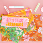 four different sized pouches which come together on a ring , one with saying "seriously?", one green ground floral print, pink ground floral print and brown ground floral print on a pink textured background with makeup items sitting above