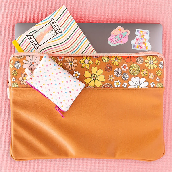 Flower Power laptop sleeve with 1/3 retro flower pattern, and 2/3 orange-brown color. There is a notebook and laptop coming out of the laptop sleeve, and a penny key ring with the tiny hearts pattern placed on top of the laptop sleeve. 