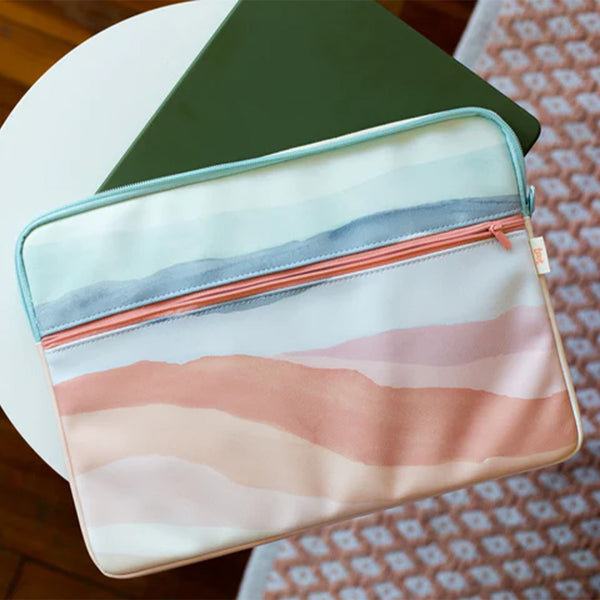 a laptop sleeve with watercolored stripes that are blue and peach. the sleeve is holding an olive green laptop and sitting on top of a white table.