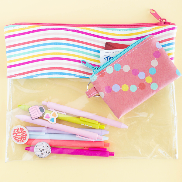 A pouch with clear vinyl and rainbow wavy line vegan leather.  There are jotter pens and enamel pins in the pouch. There is a coral colored penny pouch with a drivers license and credit card sticking out of it.  