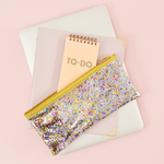 Cute pencil pouch in clear vinyl with glitter confetti, a slim design, and gold zipper on top of a macbook 