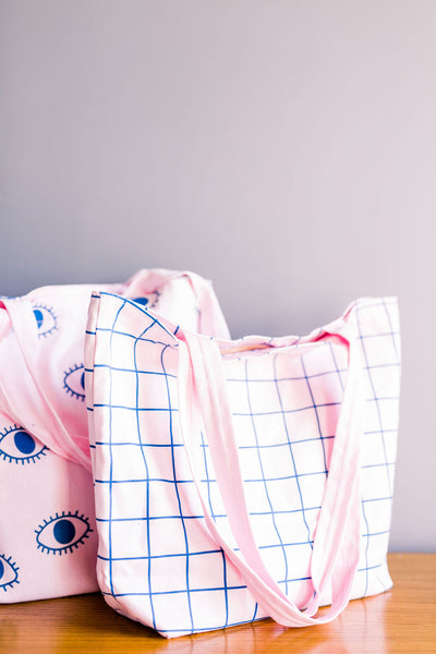 Two cute pink tote bags sitting on a table one with a grid pattern and one with eyeballs pattern.