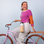 Girl on a bike wearing a daisy checker reversible simple hydration sling and a light blue background