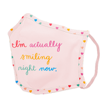 A pink facemask with rainbow themed tiny hearts on the edges, with "I'm actually smiling right now" written in color alternating scripts. 