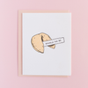 White greeting card with a fortune cookie. The cookie has a piece of paper sticking out of it with the text 