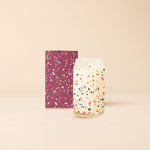 A confetti speckled 12 oz. candle displayed with the packaging. Packaging box is maroon with multicolored speckling. 