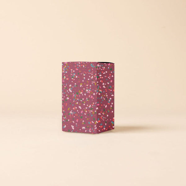 Candle packaging box that is maroon with multicolored speckling.