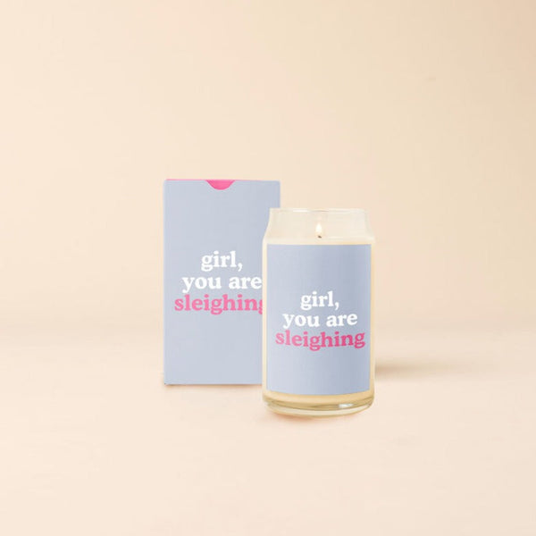 A 12 oz. candle with a periwinkle colored decal and the phrase, "girl, you are sleighing." Also displayed with packaging box that is designed the same as the candle decal.