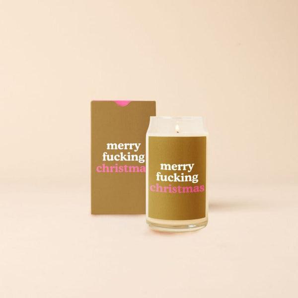 A 12 oz. candle with a tanish-brown decal with the phrase, "merry fucking christmas." Candle is displayed with packaging box designed the same as the candle decal.
