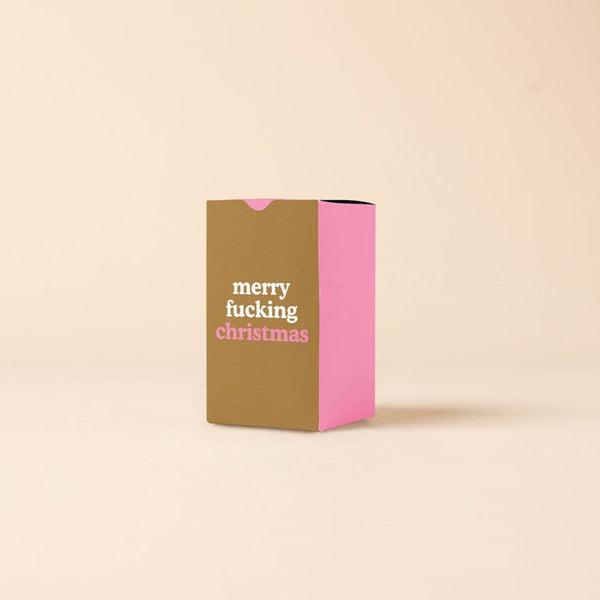 A candle box with three pink sides and a tanish-brown side that says, "merry fucking christmas."