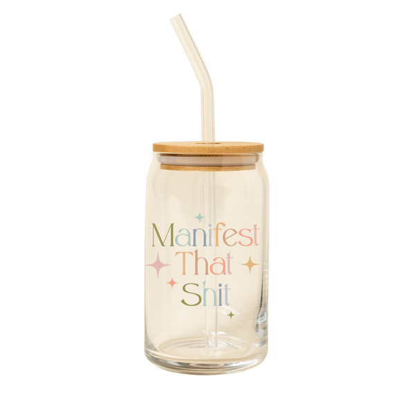 A 16 oz can glass with a glass straw. "Manifest That Shit" is printed on the front in multi-color font, with minimalist sparkle-stars surrounding the text.