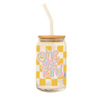 A 16 oz can glass with a glass straw; yellow checker print wraps around the glass. "One of a Kind" is printed on the front in a blue font with pink outline.