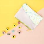 Pink and paint splatter pouch with gold zipper and tiny candies spilling out on a yellow and pink background.