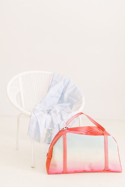 Cute tote bag in rainbow ombre print sitting next to a white chair with a blue blanket.
