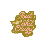 Olive green sticker with light pink lettering saying "bat shit crazy" with ombre yellow to white bat and star sparkles.