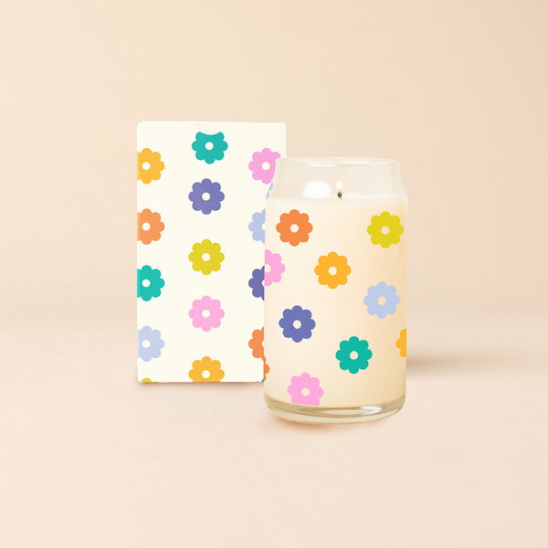 Can glass candle with illustration of multi-color daisies that wrap around the glass. Box packaging with same design sits behind candle.