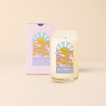 Can glass candle with multi-color flowing river into sunset. Text under river design reading "GOOD VIBRATIONS" surrounded by minimalist clouds. Pastel purple box packaging with same design as candle.
