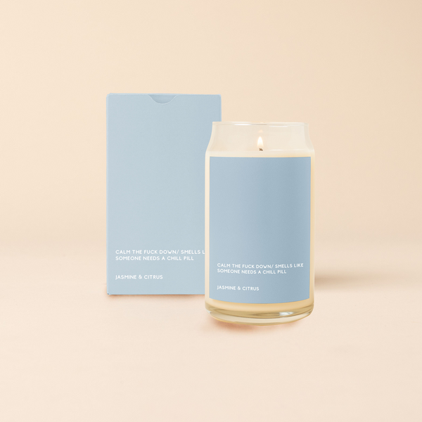 A 16oz. candle with a dusty blue decal that says, "CALM THE FUCK DOWN/SMELLS LIKE SOMEONE NEEDS A CHILL PILL" in white text on the bottom. Scent is Jasmine & Citrus.