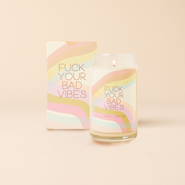 A 16 oz. candle with a multicolored decal with wavy lines. Decal says, "FUCK YOUR BAD VIBES" and the scent is Neroli & Sea Salt.