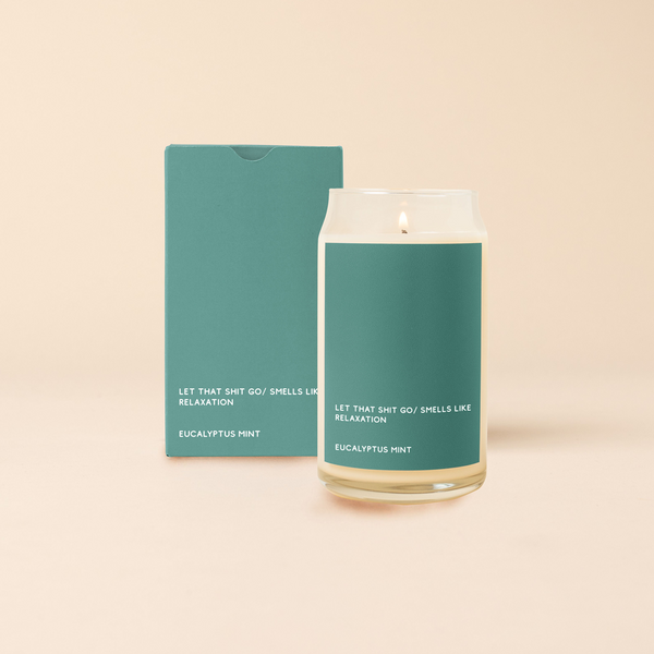 A 16 oz. candle with an emerald green colored decal that says "LET THAT SHIT GO/SMELLS LIKE RELAXATION" on the bottom. Scent is Eucalyptus mint.