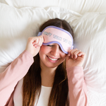 Girl laying in be with her pink and purple "Don't Talk To Me" sleep mask over her eyes.