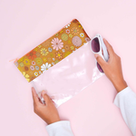 Girl holding sides of Flower Power Dollface pouch with white shades in right hand. Pouch is a cute for pencils or cosmetics with floral print vegan leather at the top and clear vinyl on the bottom. 