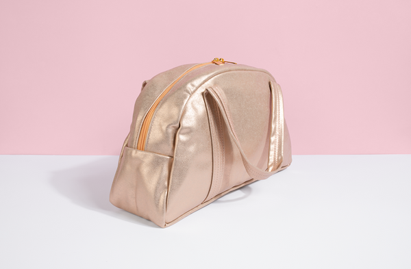 Cute handbag in gold metallic vegan leather and a zippered top on pink and white background. 