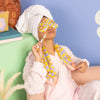 Girl relaxing with a cool funky daisy weighted eye pillow and neck wrap on a couch with a blue background and smiley tote and dweedle dee pouch in the background.