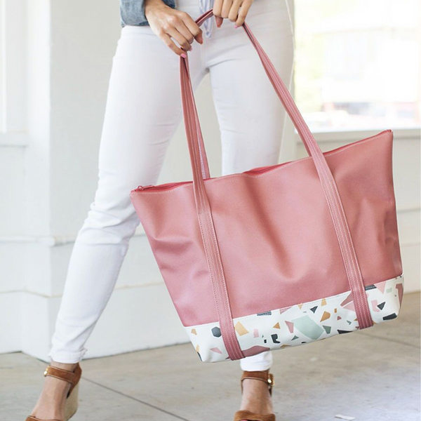 Girl in white jeans holding a cute travel bag in red and terrazzo vegan leather and zippered top.
