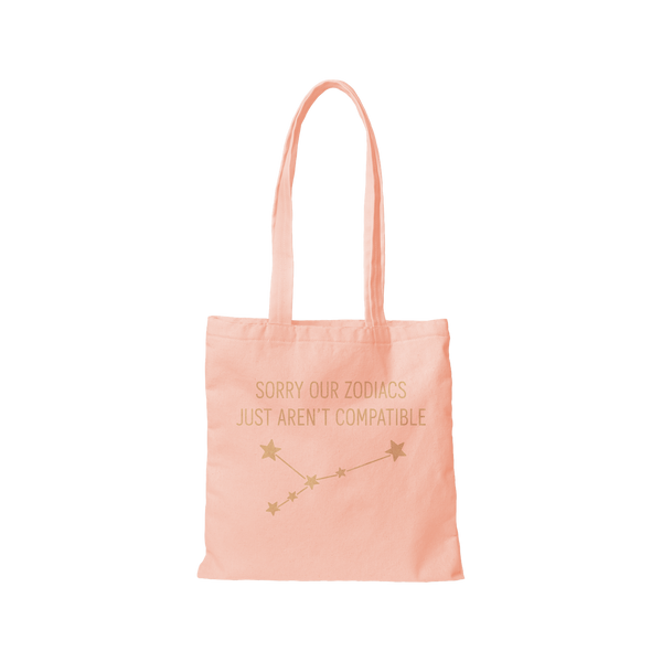 A Pink-toned colored canvas tote bag with the phrase "Sorry our Zodiacs just aren't compatible" printed on the front. A constellation of stars in printed underneath the phrase.