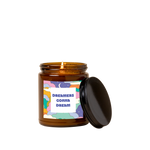 Amber glass candle jar with sticker on front with illustration of multi-colored clouds and stars + moon and text that reads "DREAMERS GONNA DREAM" in blue font in a white square.