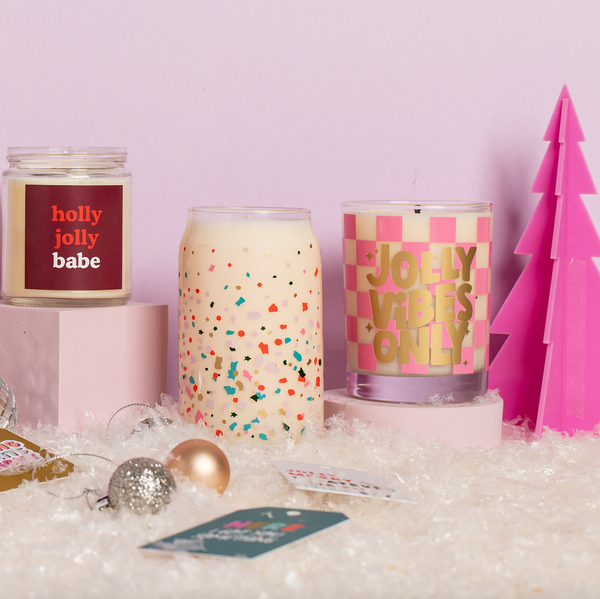 Three Holiday TOOT Candles, one Rocks Glass, one 12 oz. and one Yippie,being displayed with a pink acrylic tree decoration and small ornaments.