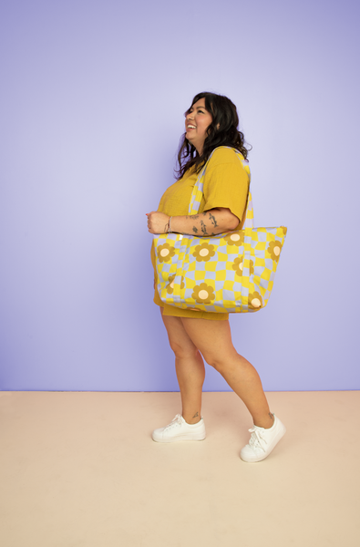 Girl wearing the cool funky daisy weekender tote. Periwinkle color background. 