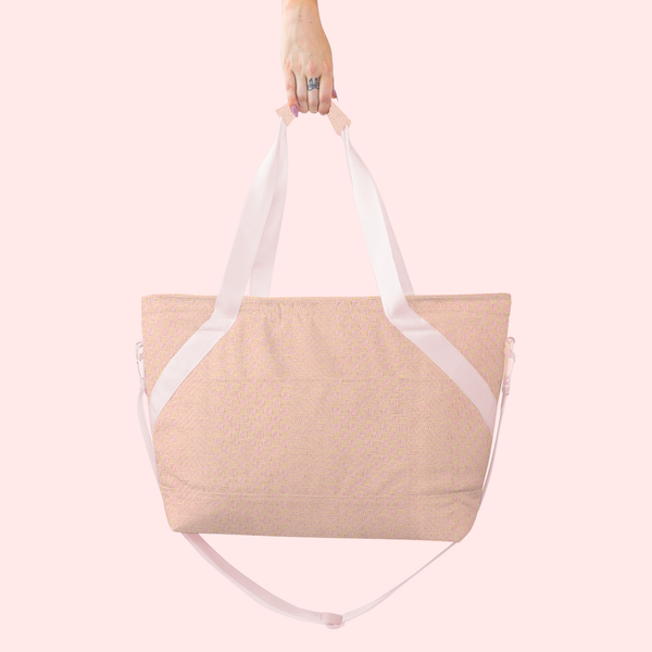 A pink and cream cross stitched tote bag with light pink straps. Bag is being displayed in front of a light pink background.