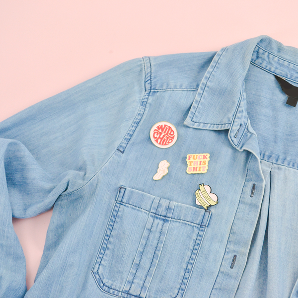 Our cute enamel pins pinned to a chambray denim shirt. Wild child, fuck this shit, so many feelings, and our confetti hand are the pins used in this picture.