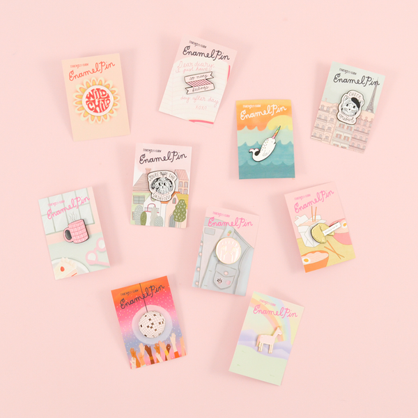 Several of our cute enamel pins on a pink background