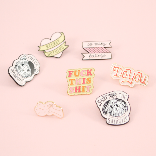 Several of our cute enamel pins on a pink background