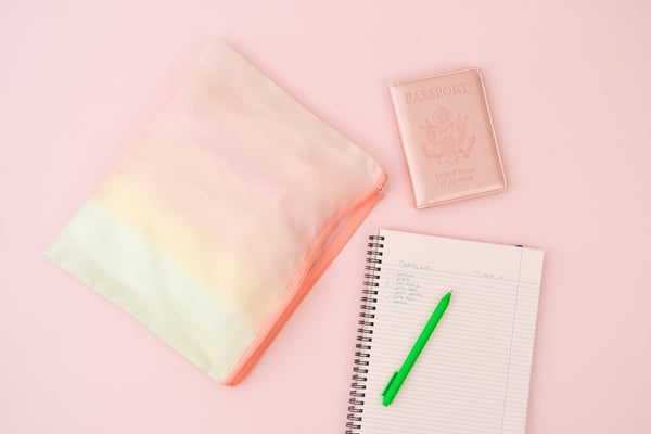 a ripstop pastel gradient pouch next to a notebook, green grass jotter, and a rose gold passport holder