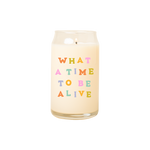 A 16 oz. candle with "What a time to be alive" printed on in multicolored lettering.