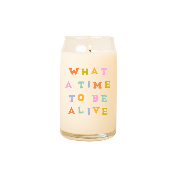 A 16 oz. candle with "What a time to be alive" printed on in multicolored lettering.